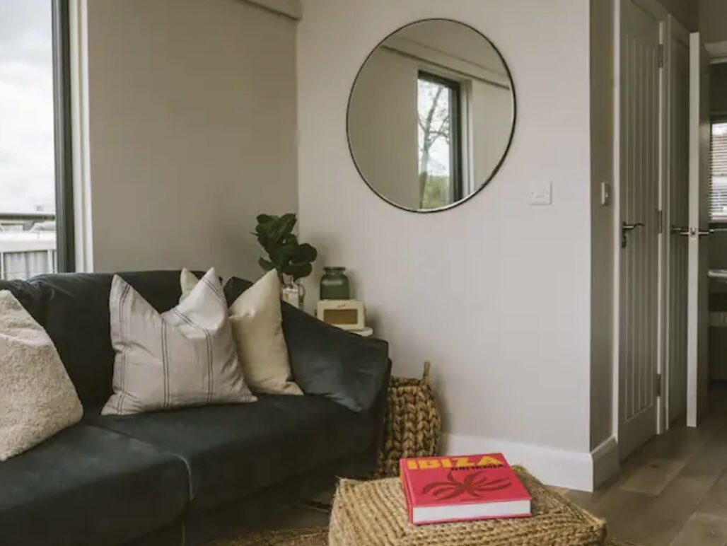 Living area with sofa, cushions and table with book and circular mirror on the wall